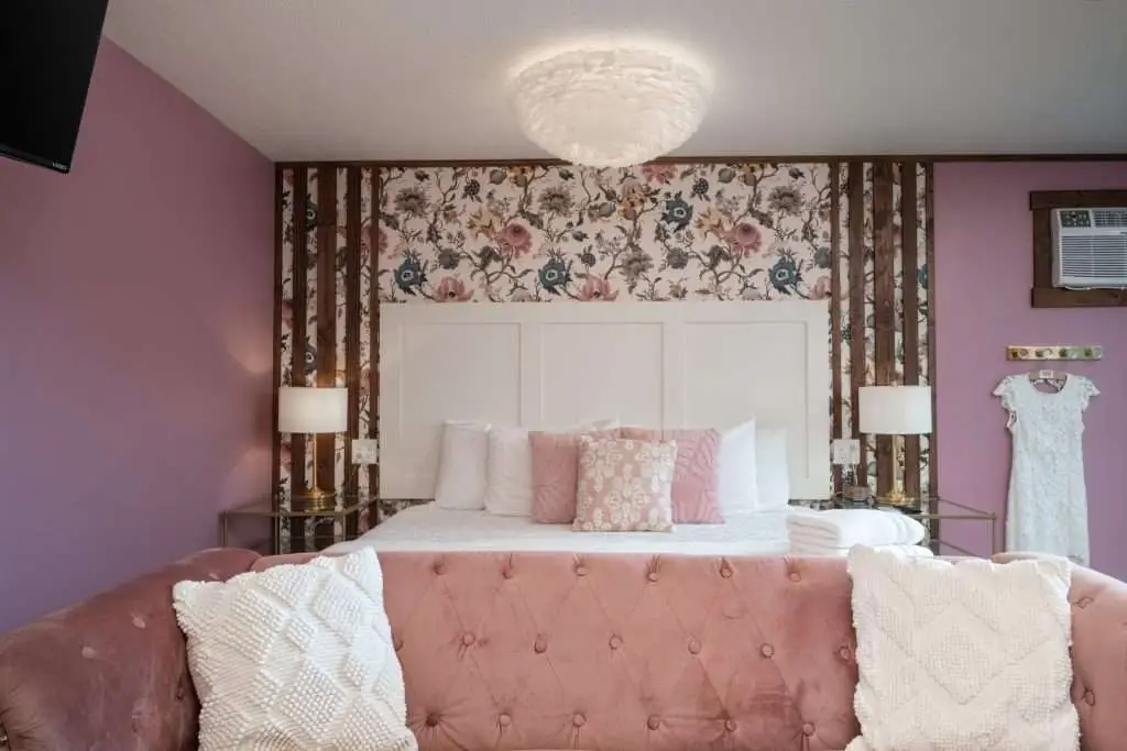 King bed with tufted pink bench and floral wallpaper